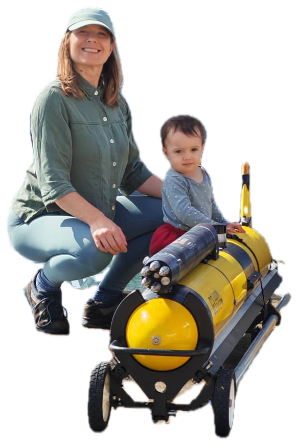 Isabelle crouching next to a yellow ocean glider on its trolley, with her toddler sitting on the glider